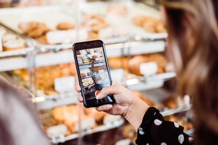 Woman taking a photo of items in a bakery to simulate how a diary study captures real user behavior.