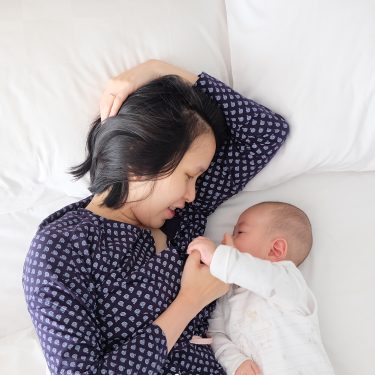 Mother laying next to her baby in bed.